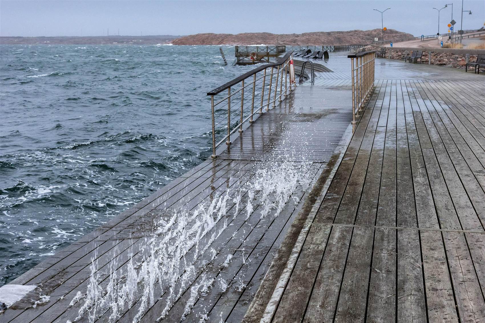 Golven slaan over een houten wandelpier tijdens een storm aan zee.